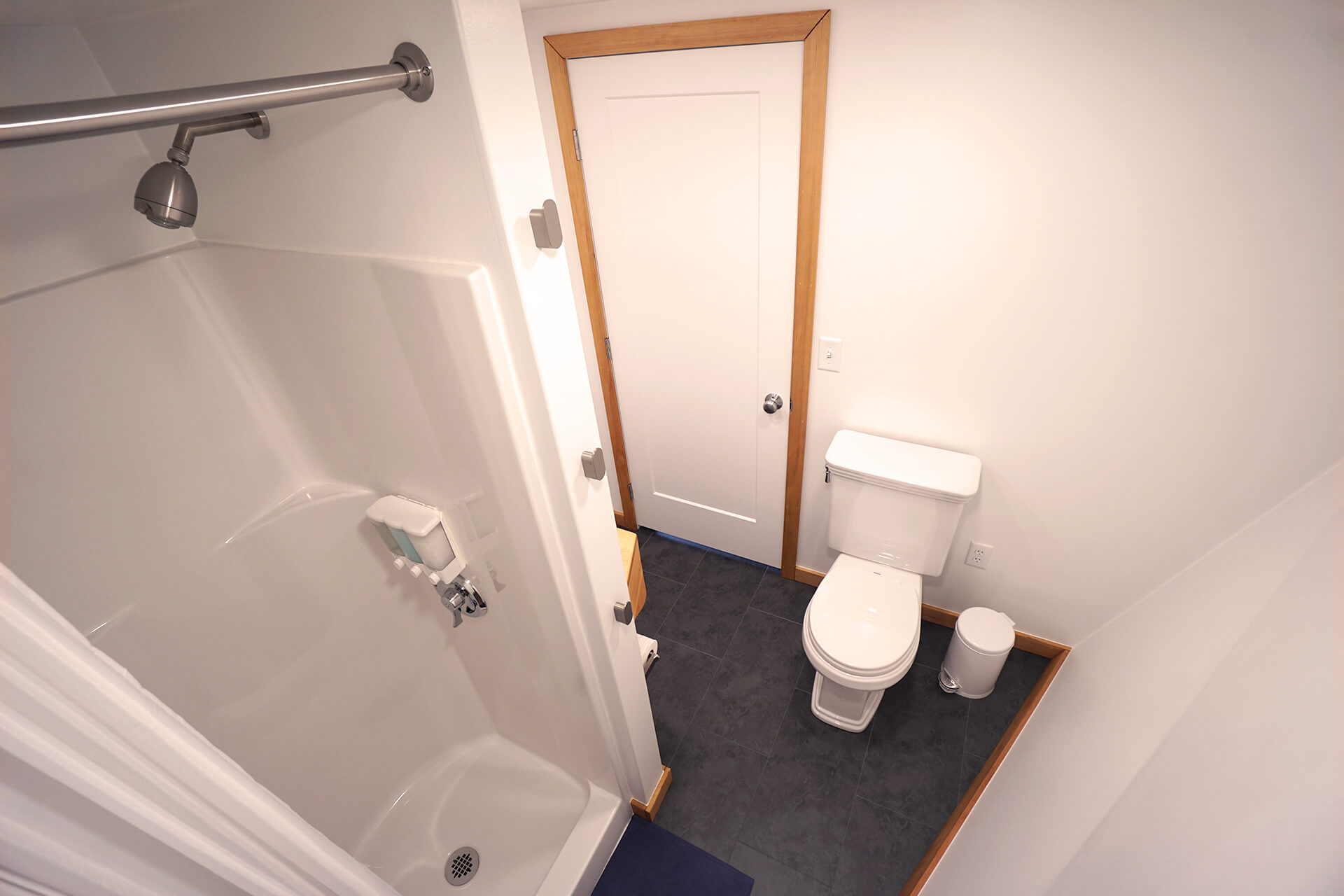 View of the bathroom from above the shower, showcasing the built-in soap, shampoo, and conditioner dispenser, along with the Toto toilet and a small white trashcan.