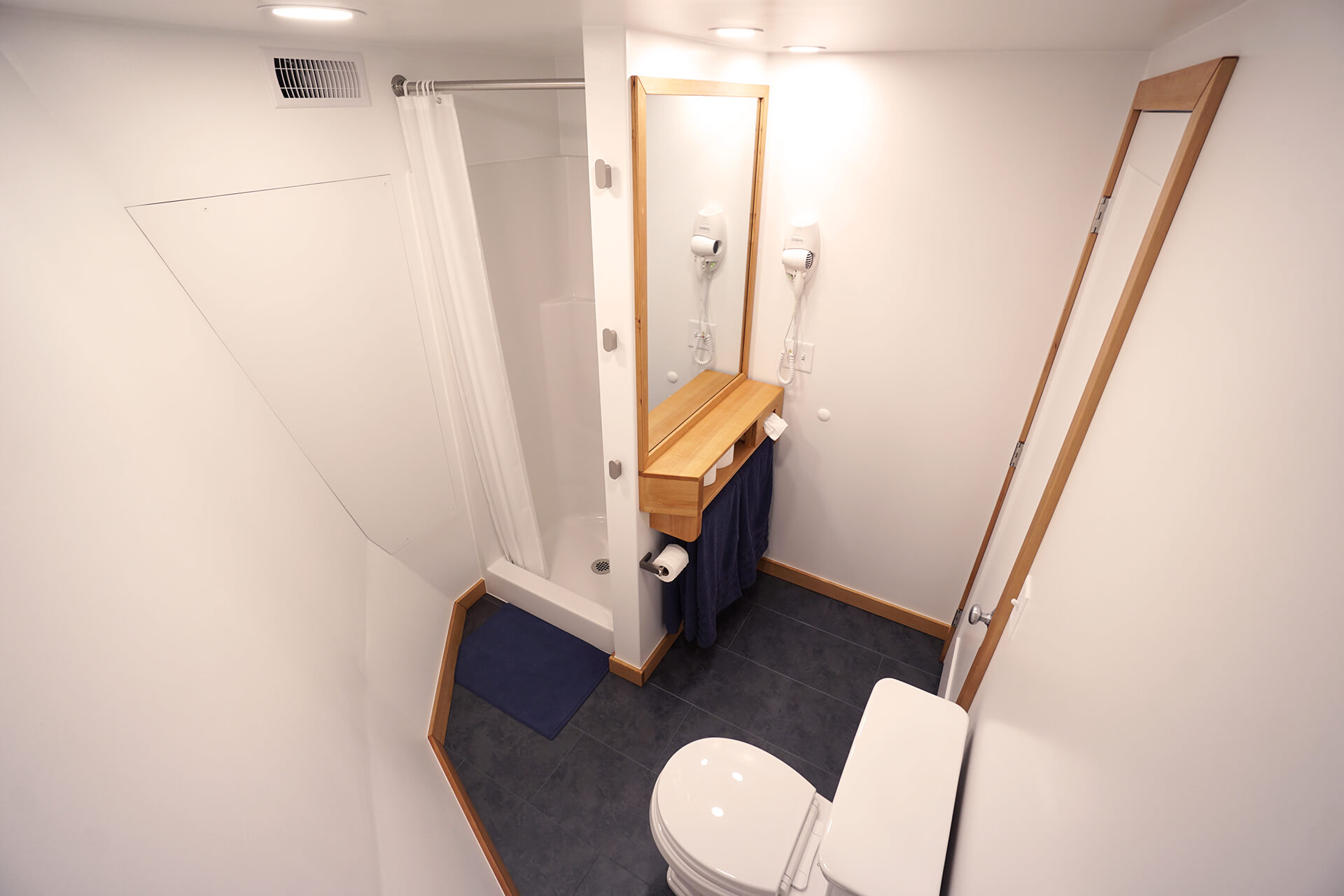 View of the white bathroom from above the toilet, highlighting the large wall-mounted mirror, towel rack, and built-in hair dryer.