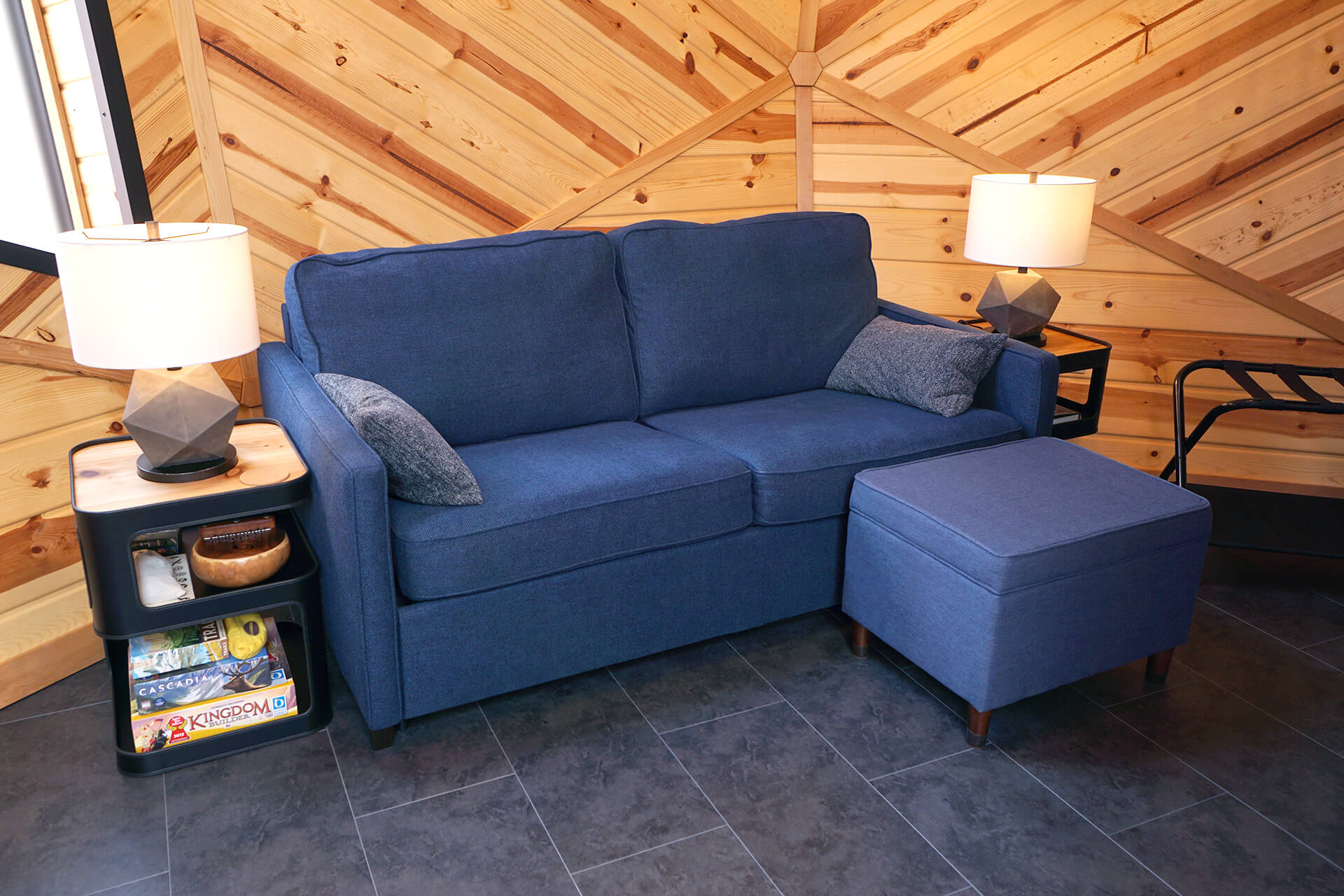 The living area featuring a blue couch and ottoman, flanked by two elegant black side tables and geometric lamps.