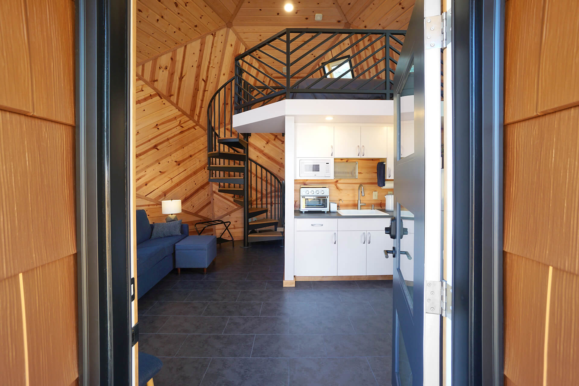 View from the front door, highlighting the aluminum shingle siding and glimpses of the interior, including the loft, kitchenette, couch, and composite slate flooring.