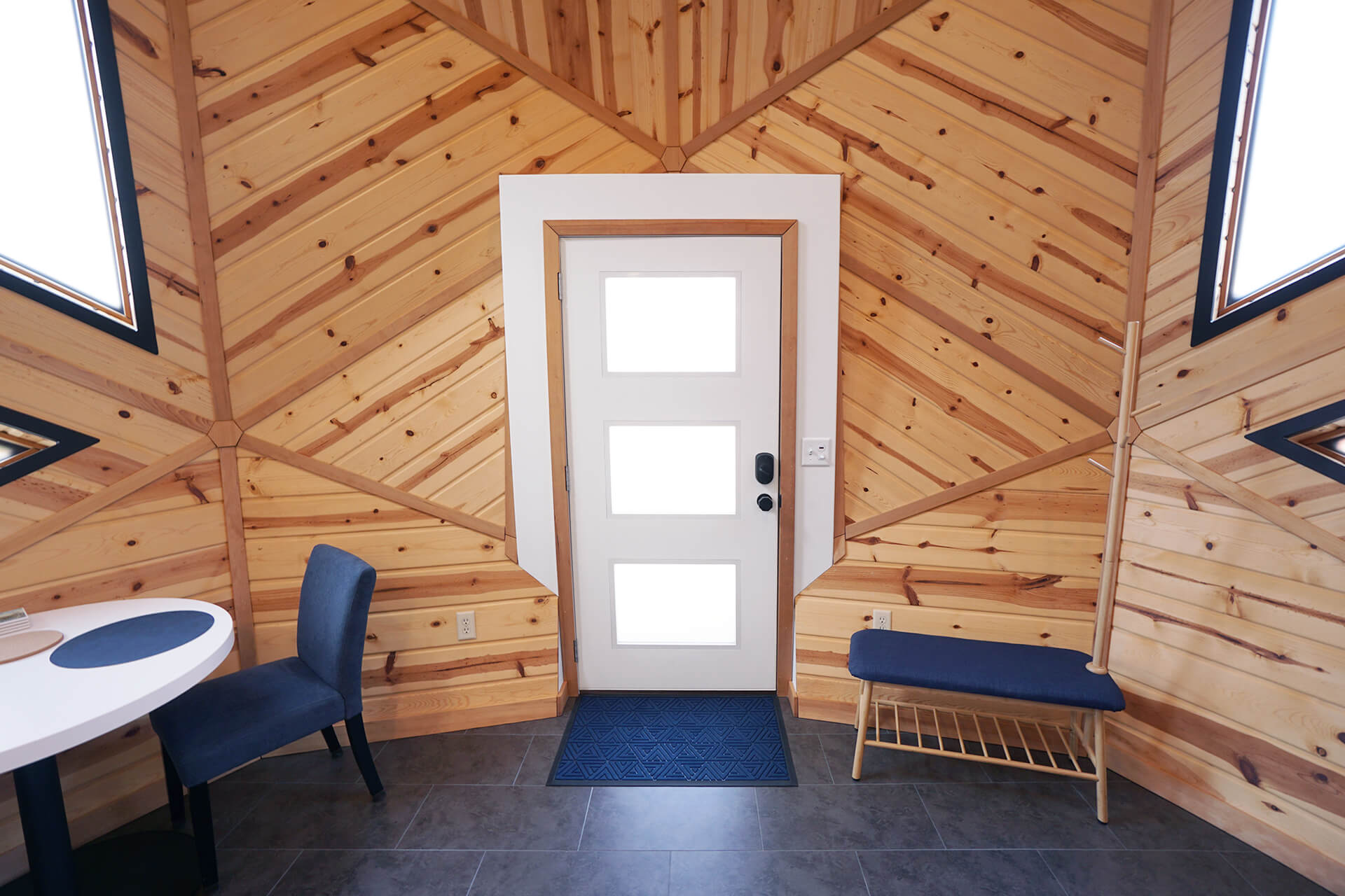 Center view of the entrance from inside, featuring a white door with frosted windows, the dining room on one side, and a bench with a coat rack on the other.