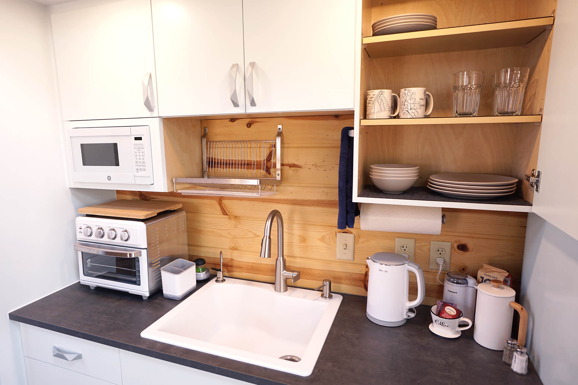 The kitchenette with an open cabinet door displaying dishware and mugs featuring custom geodesic dome drawings.