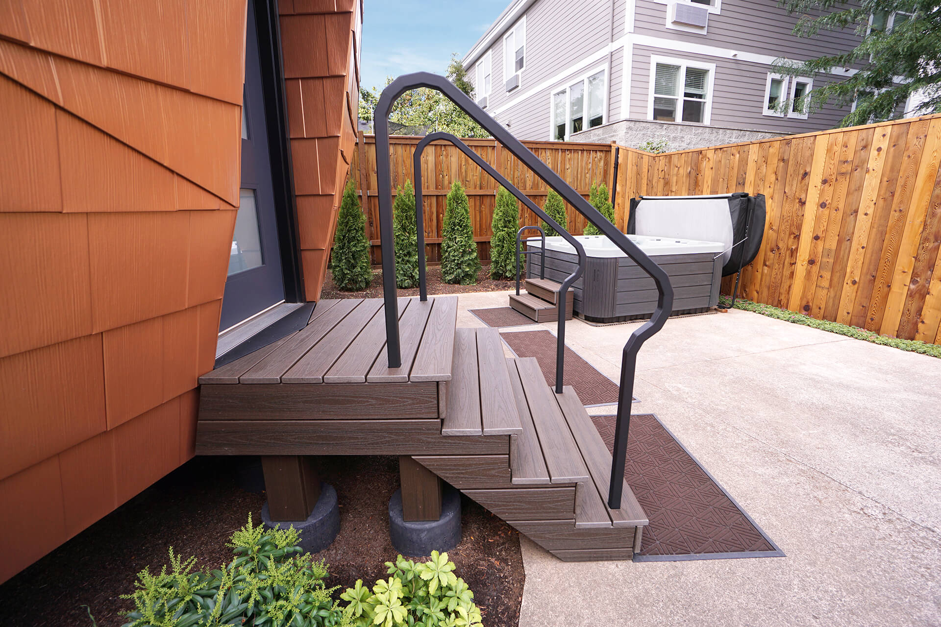 Side view of the mini geodesic dome home porch with handrails, composite decking, and a hot tub in the background.