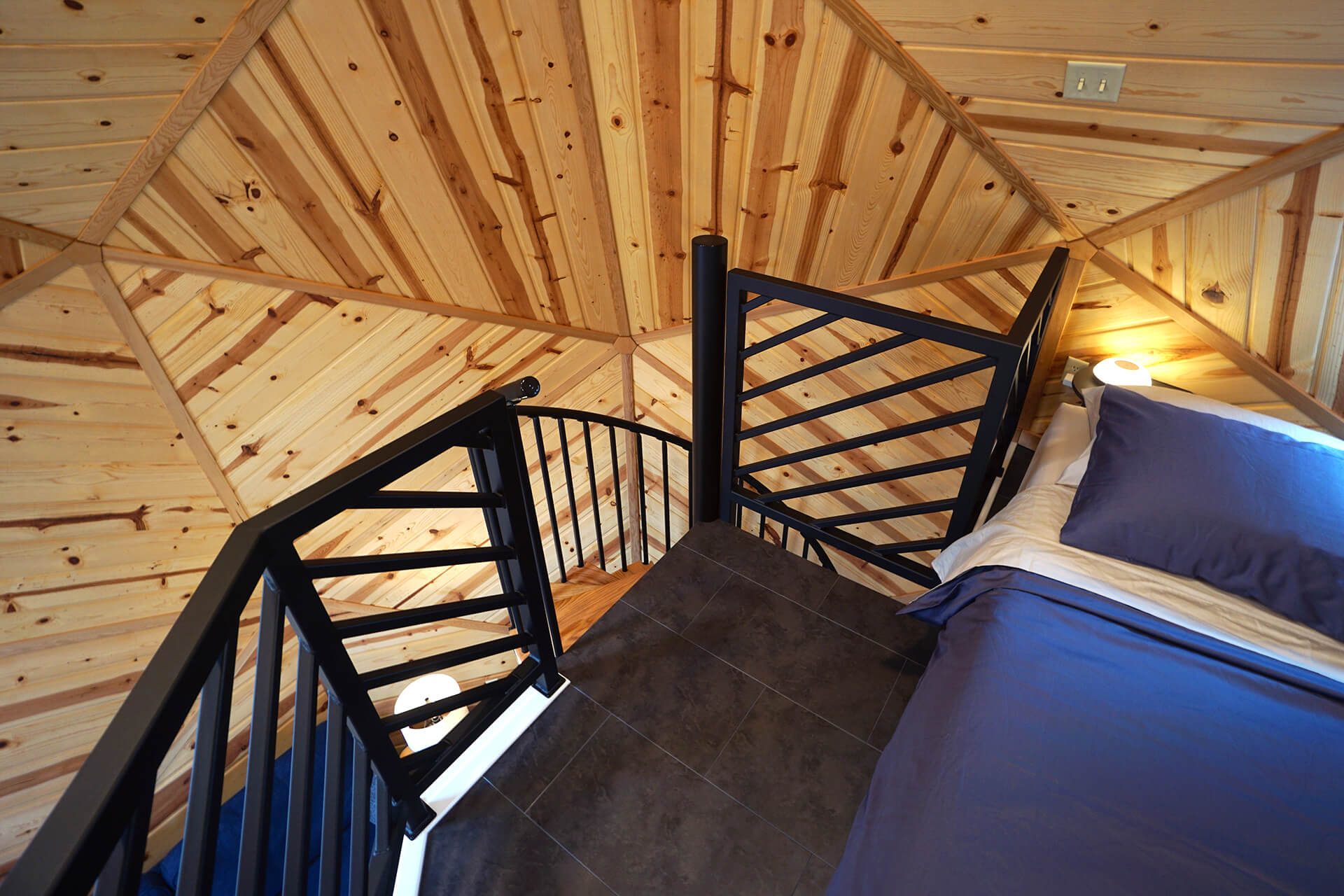 View of the loft spiral stair landing and railing, showcasing the open space around the queen-sized bed.