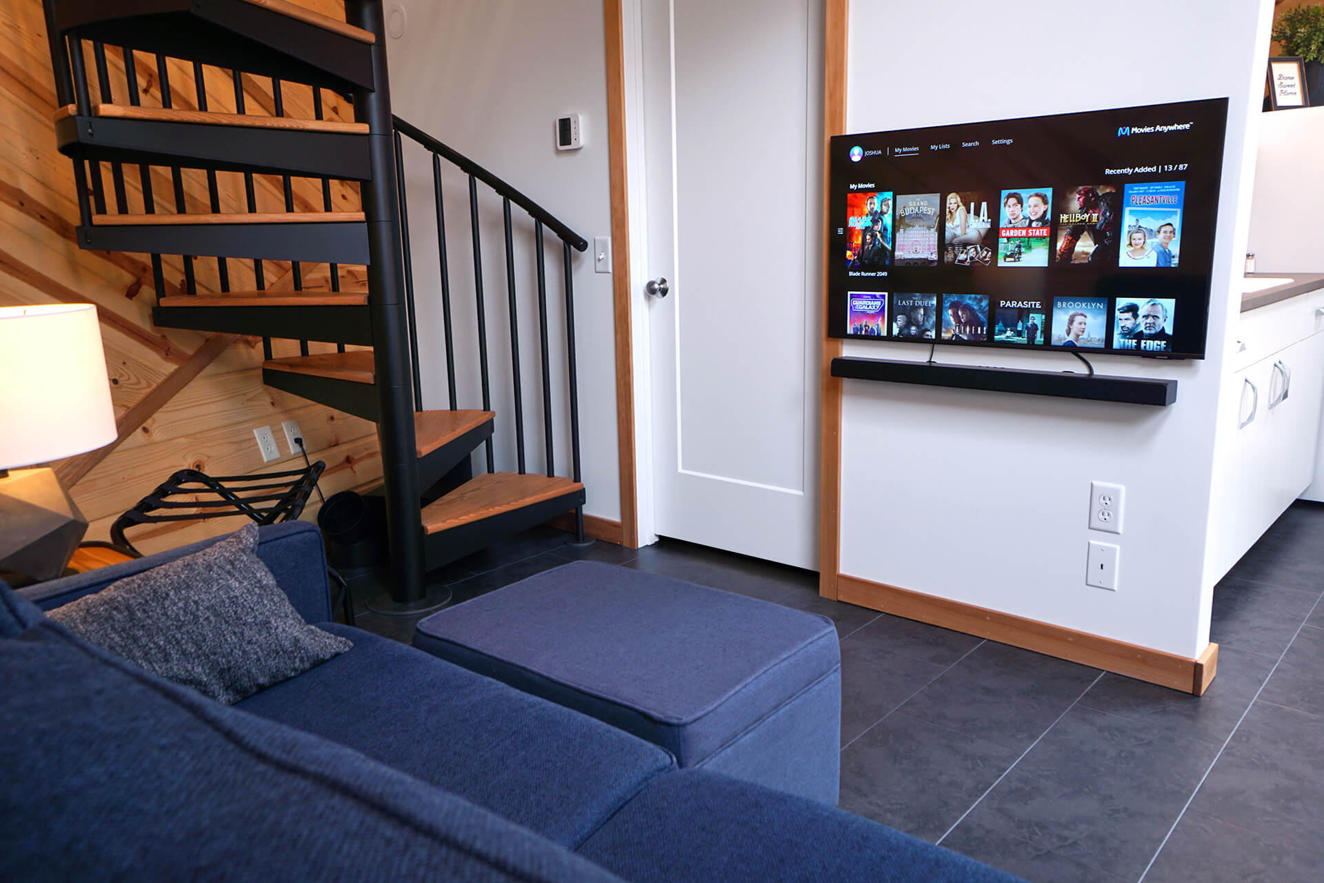 View from the couch, highlighting the wall-mounted 43-inch television, bathroom door, and HVAC thermostat.