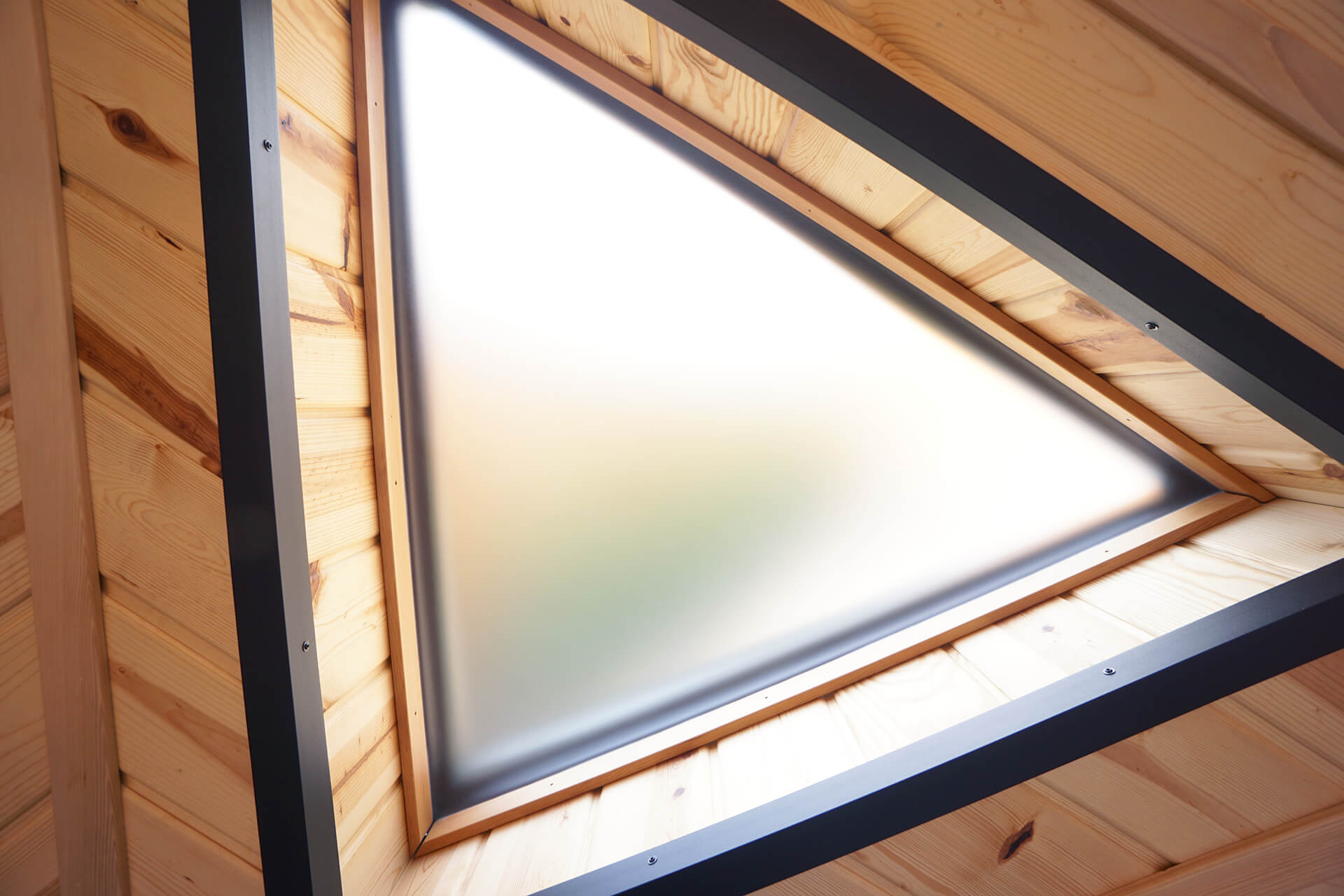 Close-up of the large triangular window with frosted plexiglass, wooden inner trim, and black powder-coated steel outer trim.